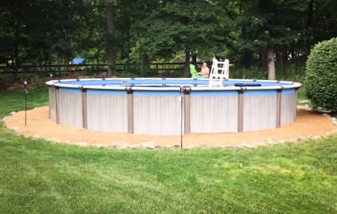 Circular above-ground pool installed in a backyard with green grass and trees surrounding it
