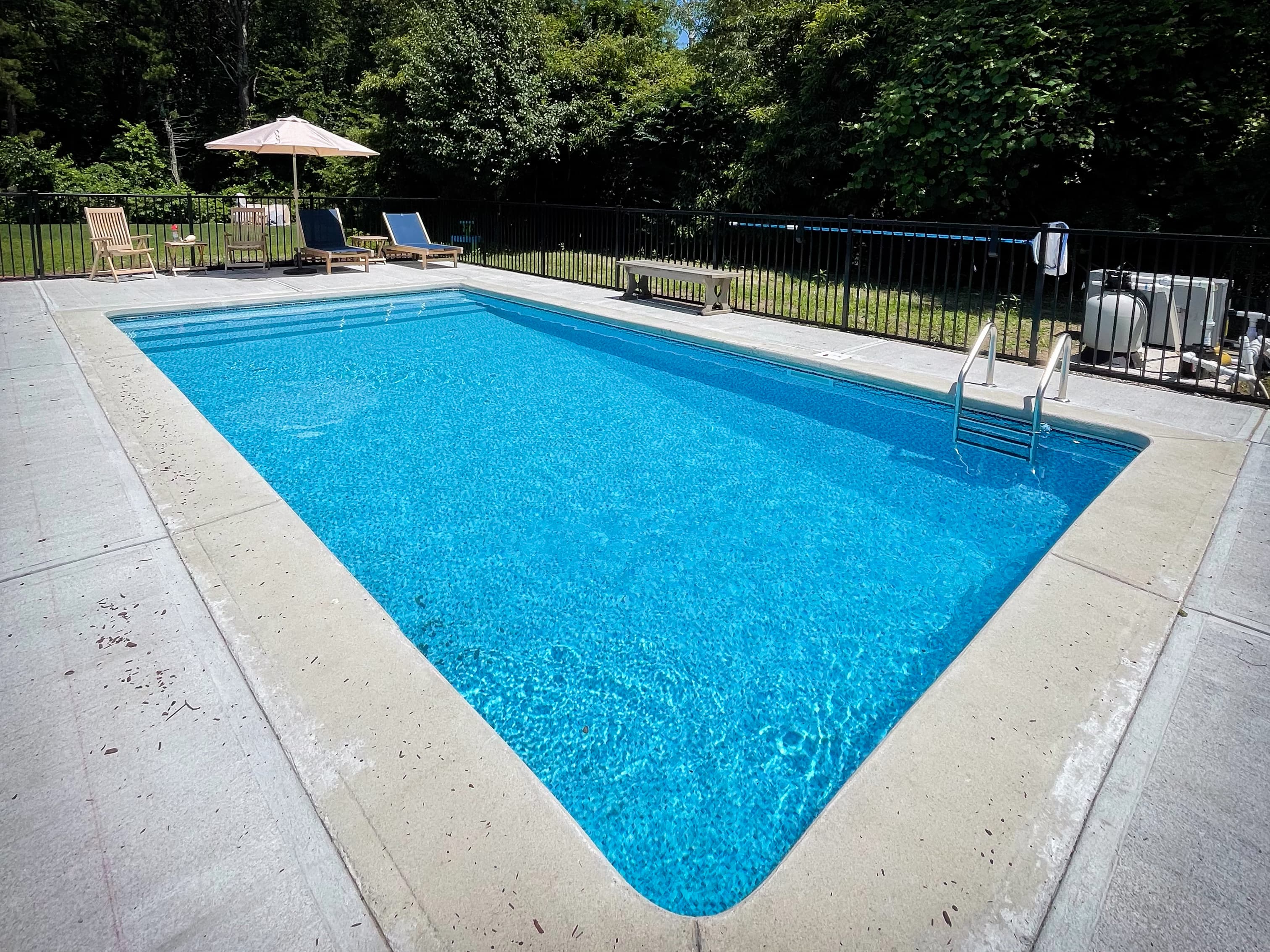 Rectangular in-ground pool with concrete surround, surrounded by wooden fence