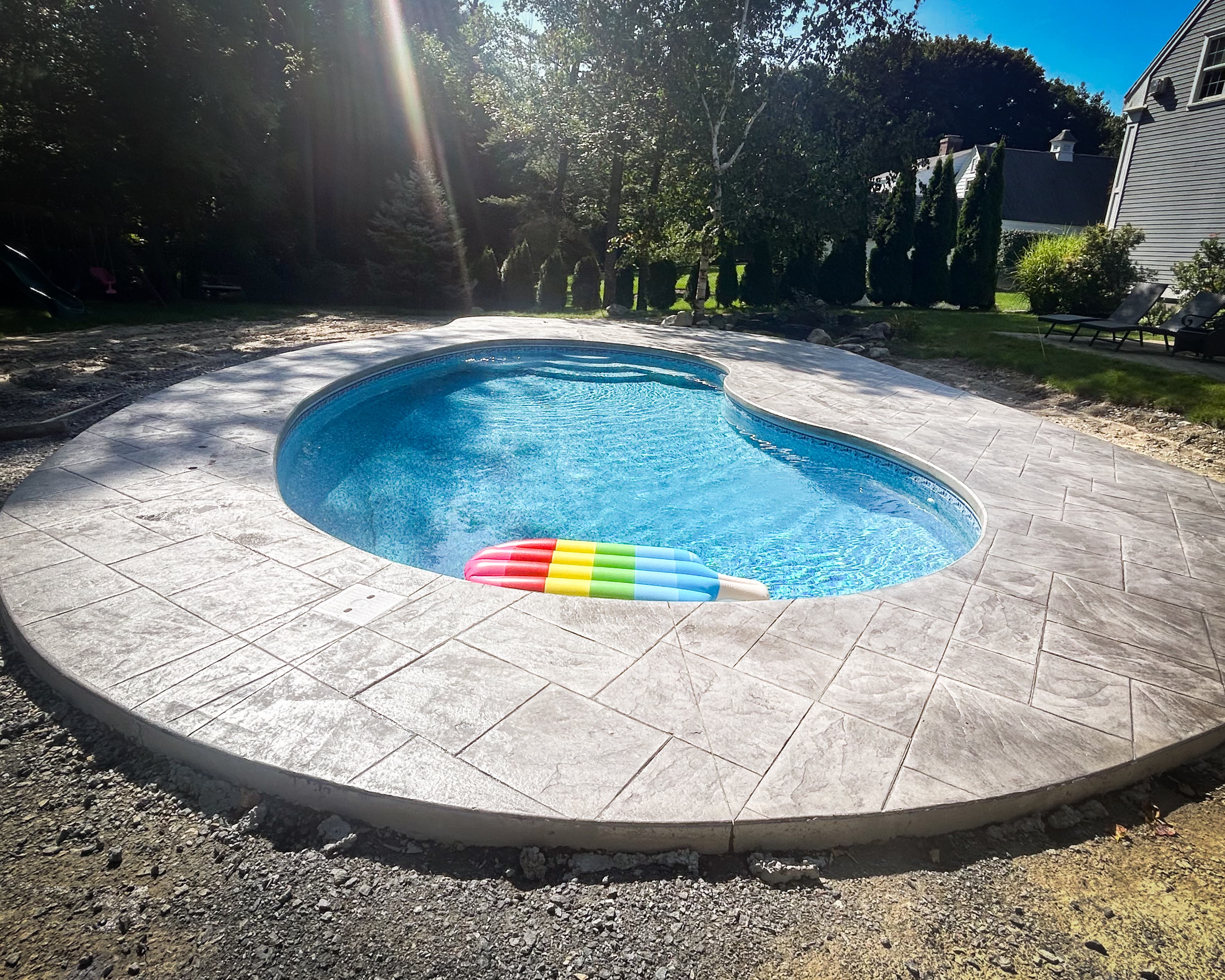 Kidney-shaped in-ground pool with stamped concrete patio, surrounded by trees