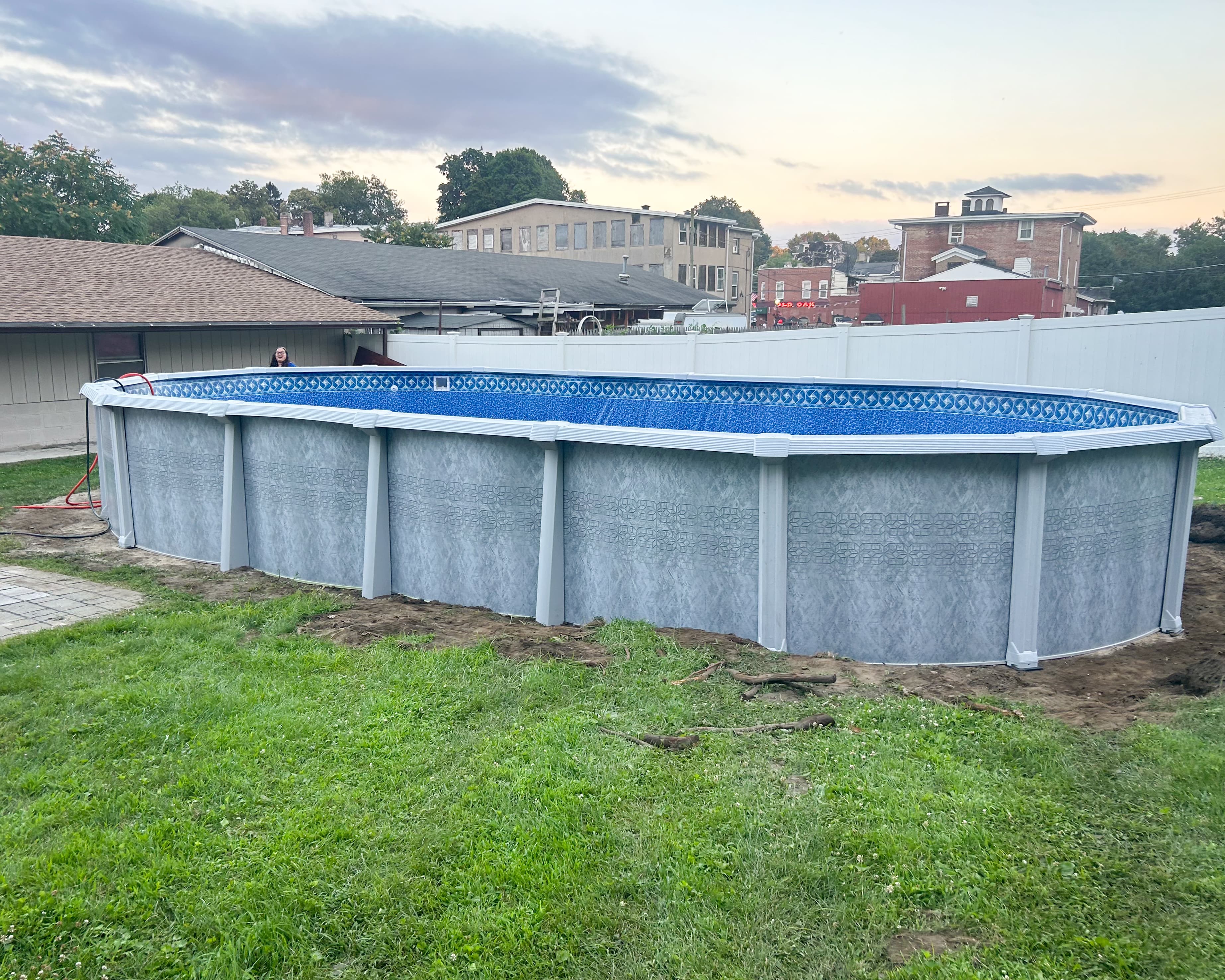 Oval above-ground pool installation on a grassy yard, with houses visible in the background
