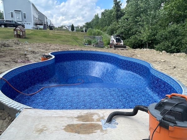 Semi-inground pool project in Worcester backyard with two-story house and trees in background