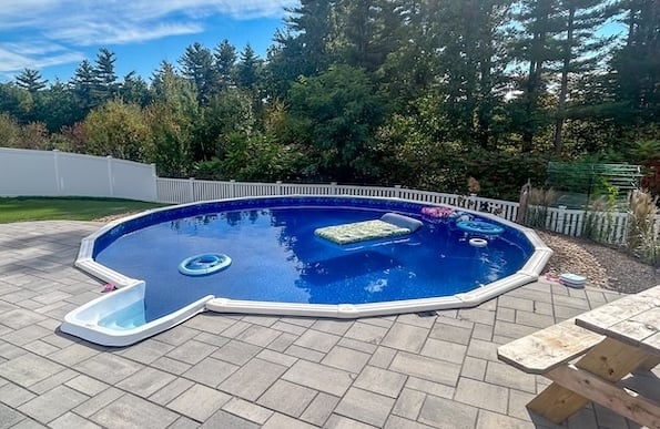 Completed round-shaped semi-inground pool with vibrant blue water surrounded by stone pavers
